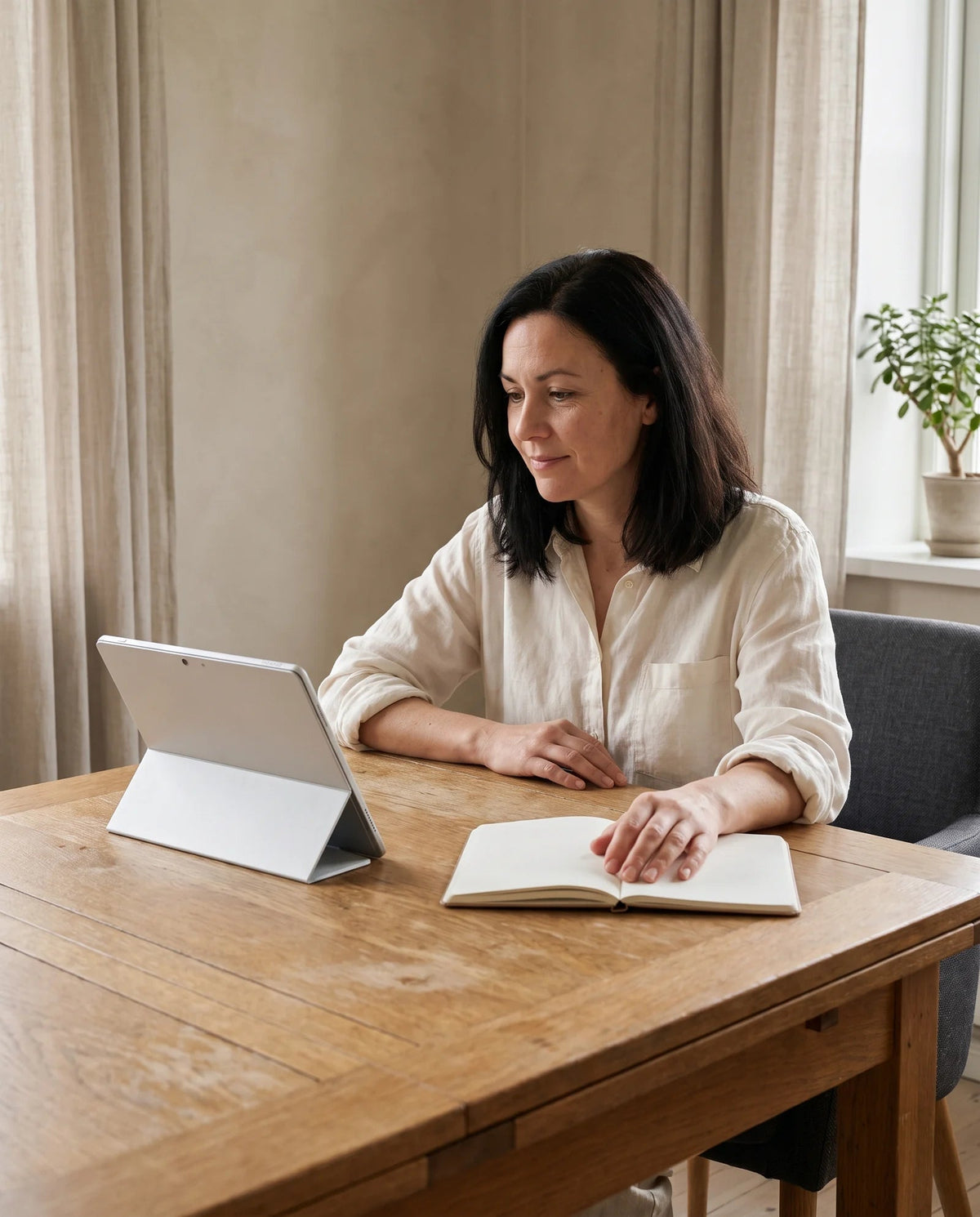 A woman watching a tablet at an oak table in a softly lit home