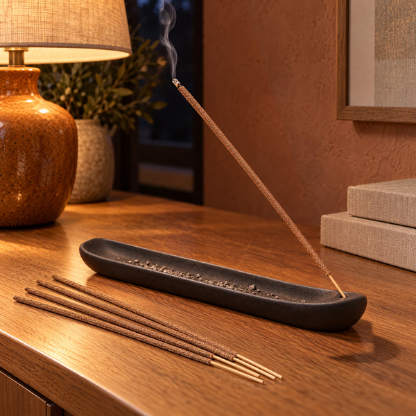 A Cinnamon incense stick smoldering in a ceramic tray on a warm evening table.
